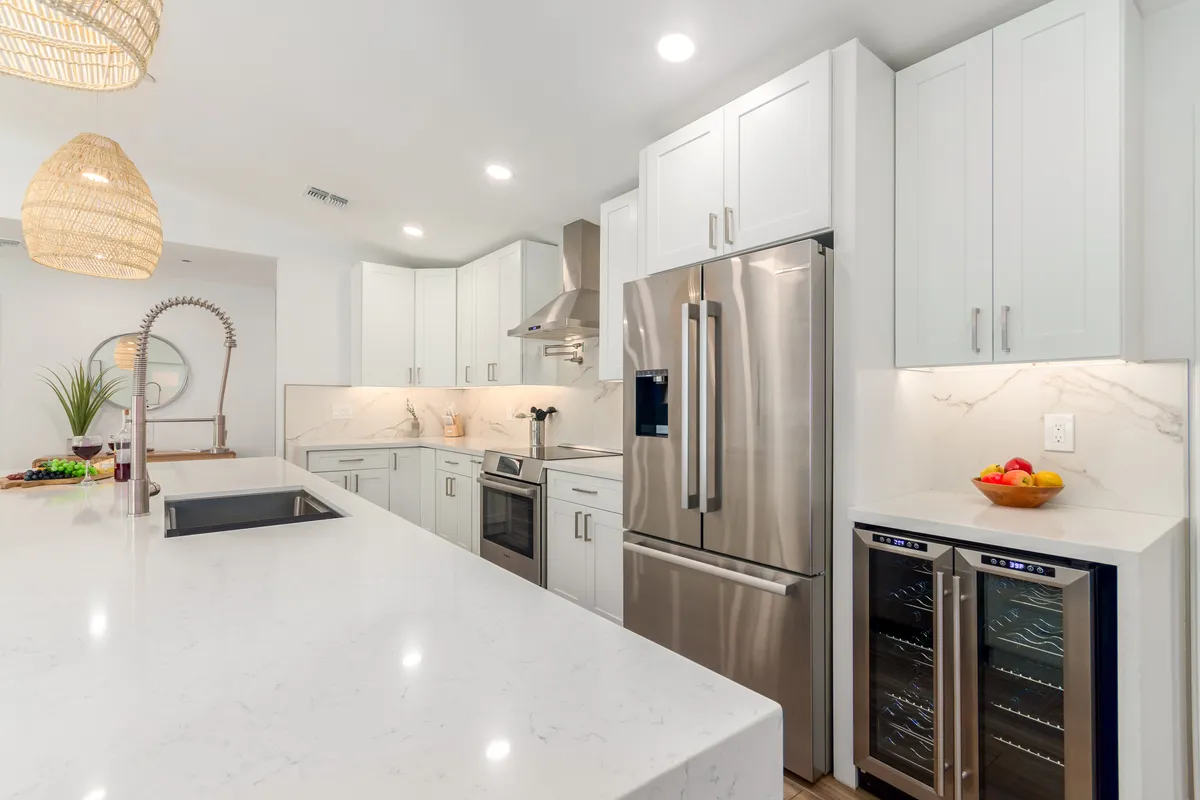 A cheerful, contemporary kitchen with a large island, stainless steel appliances, hanging pendant lights, and a bowl of fresh fruit. The layout is ideal for preparing meals as a group or enjoying the convenience of provided starter kits.