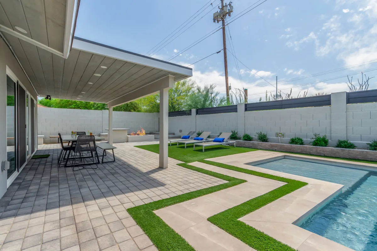 The backyard features a sparkling swimming pool surrounded by a landscaped grass area, a fire pit with comfortable patio seating, and space for sunbathing and outdoor dining. The scene is inviting, with plenty of room for family activities and relaxation in a private setting.