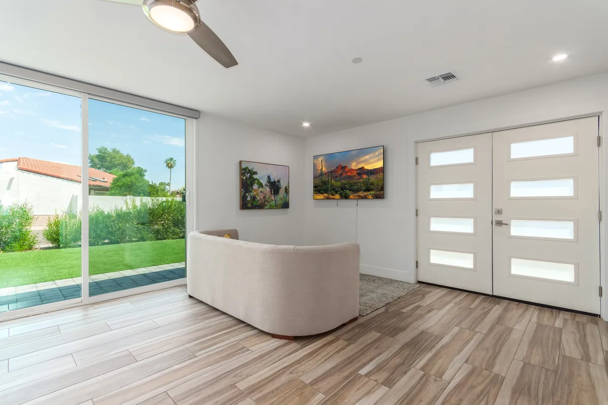 This image shows a welcoming main living area with a sofa, large windows flooding the space with natural light, engaging artwork on the walls, and a visible front door. The room exudes a sense of comfort and openness suitable for family gatherings or relaxing after an adventure.