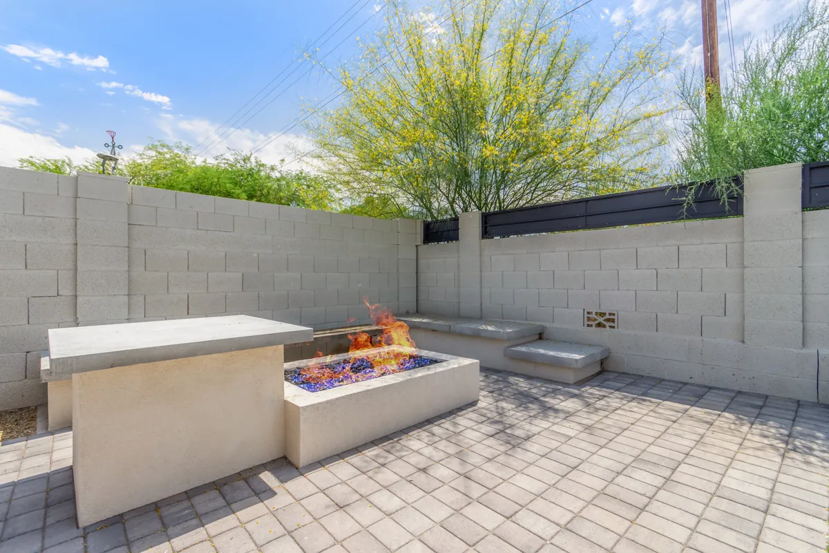 This exterior shot features a modern fire pit with concrete seating, surrounded by lush landscaping. The setup is perfect for evening get-togethers, cozy conversations, or unwinding with a glass of wine under the stars, creating an atmosphere of warmth and comfort.