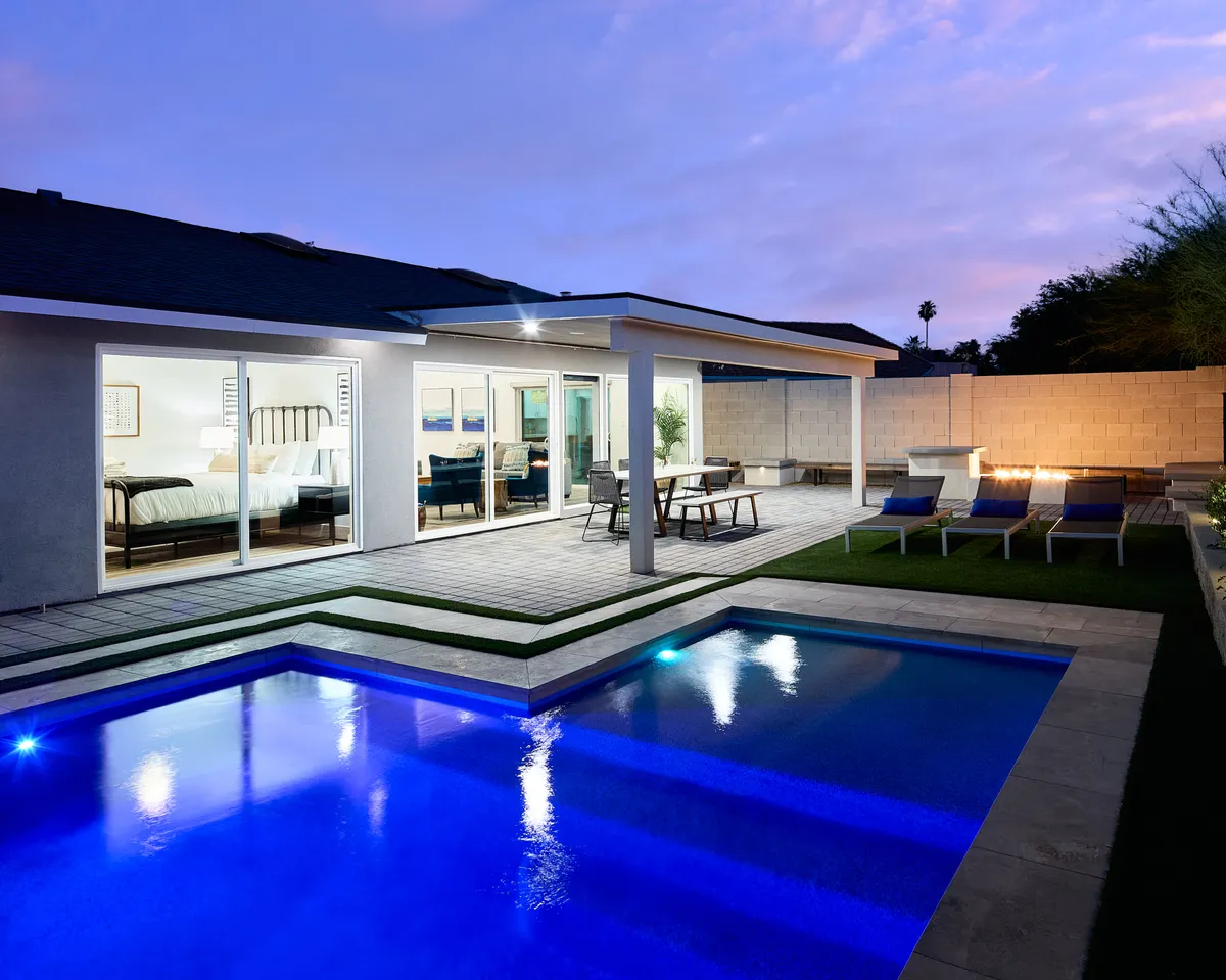 This image showcases an inviting backyard with a sparkling swimming pool, surrounded by an outdoor seating area and large glass doors that hint at seamless indoor-outdoor living. The space is well-appointed for both relaxation and social gatherings, with ample room for sunbathing, lounging, or outdoor dining under the Arizona sky.