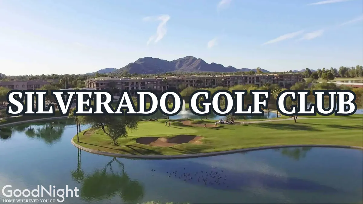 A wide view of a picturesque golf course framed by a calm lake and distant mountains. The course is lush and green, with the clubhouse visible and tranquil water reflecting the sunset. The setting is peaceful, inviting, and hints at the renowned golf experiences available nearby.