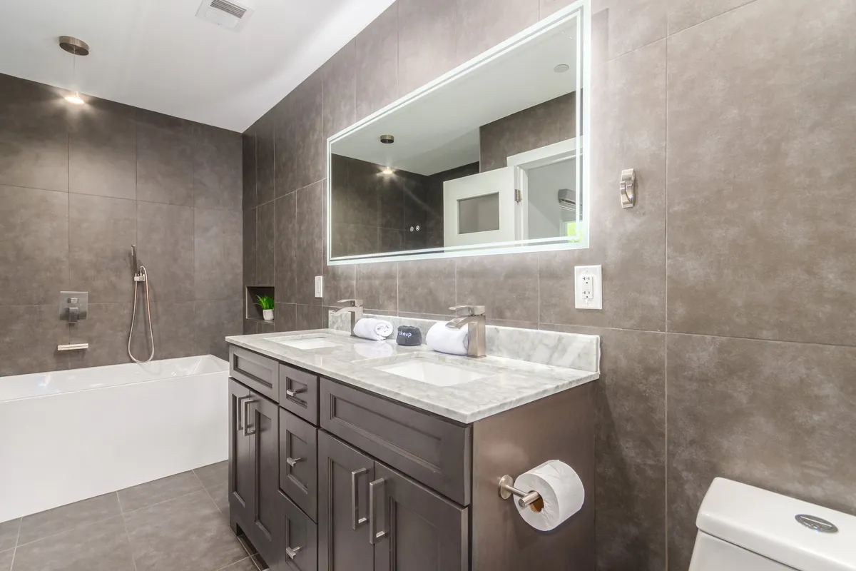 A modern bathroom with a double sink vanity, expansive mirror, soaking bathtub, and elegant fixtures. The space exudes a spa-like, calming feel—perfect for unwinding after a day out.