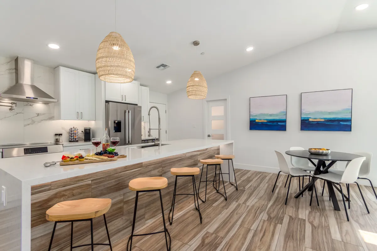 A welcoming kitchen and dining area featuring a central kitchen island with hanging light fixtures, artwork on the walls, and a dining table nearby. The layout is open and inviting, perfect for sharing meals and conversations.